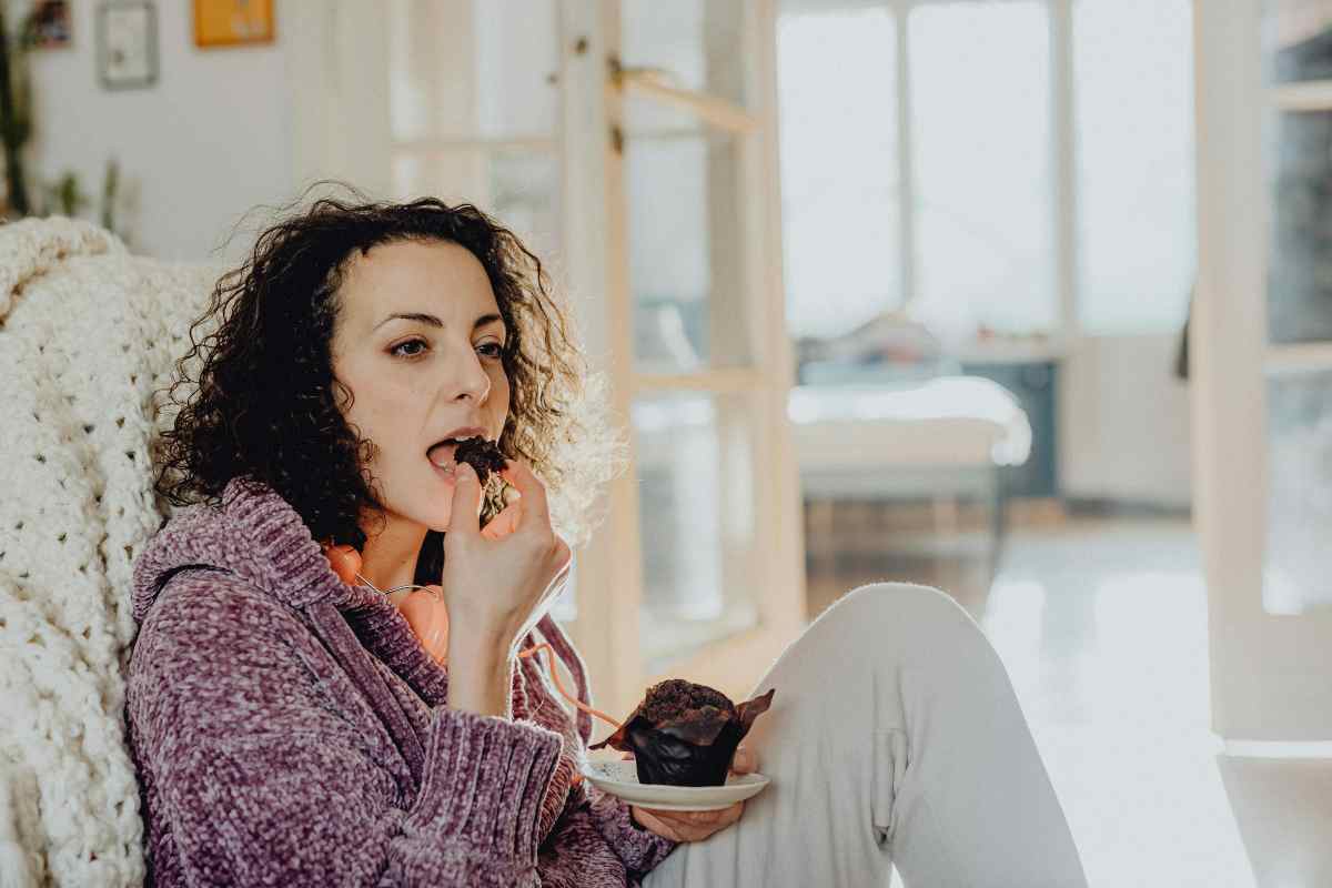 donna seduta in poltrona che mangia un muffin al cioccolato