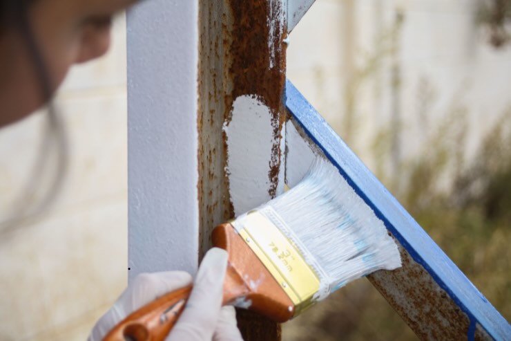 mano di donna con pennello e vernice che pittura barra di ferro di ringhiera