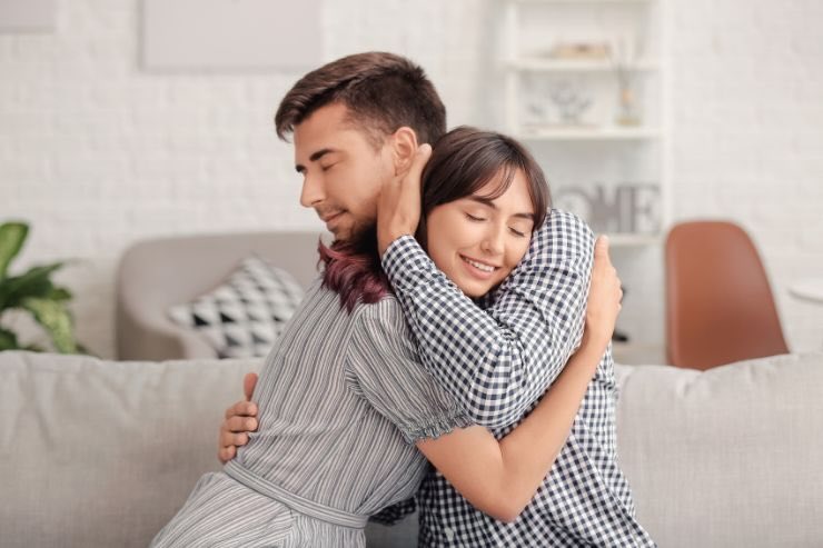 Uomo e donna si abbracciano sorridenti sul divano, occhi chiusi 