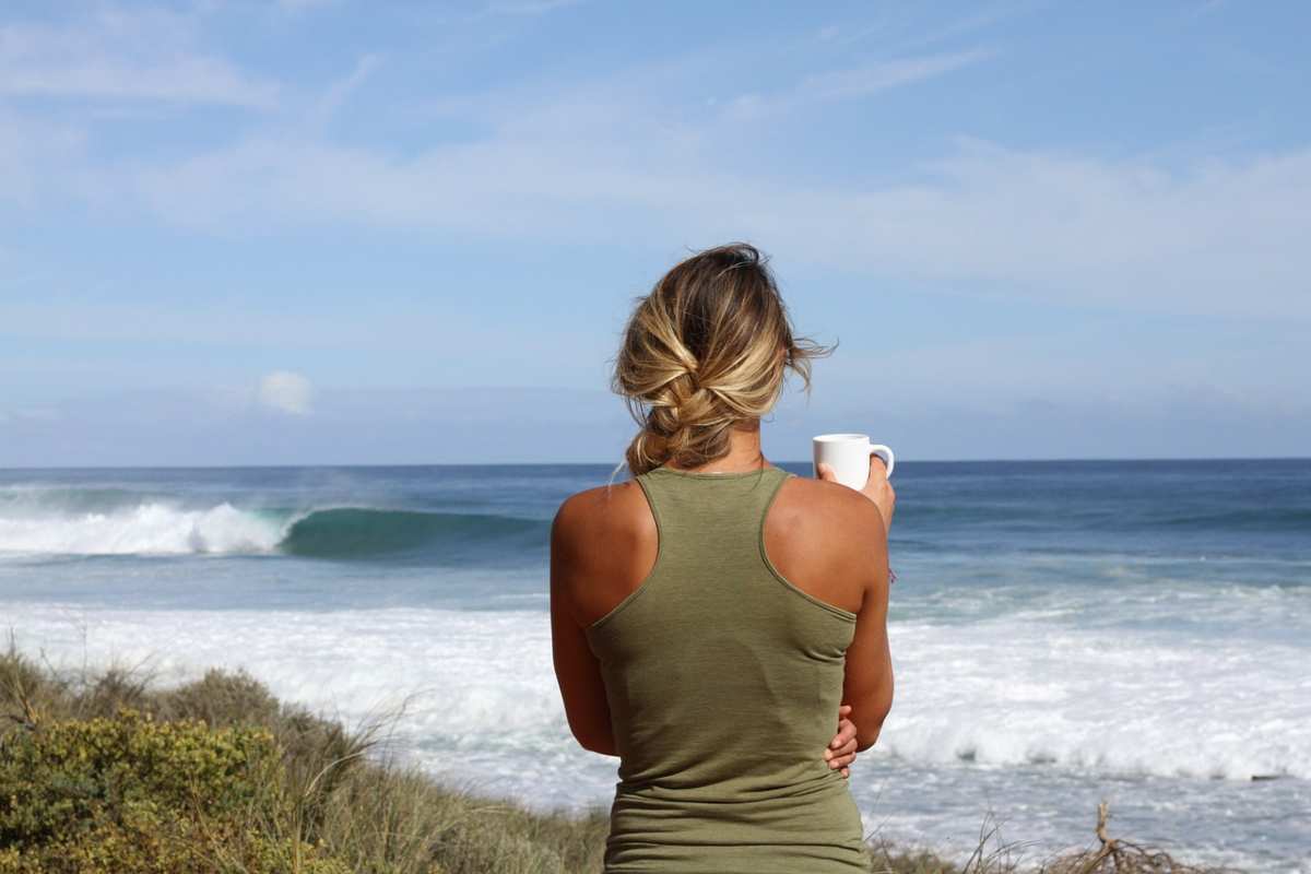 donna di spalle con una tazza in mano che guarda il mare