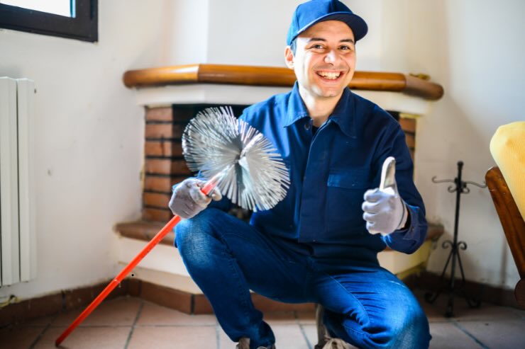 spazzacamino con cappello sorridente e pollice in alto e sullo sfondo camino