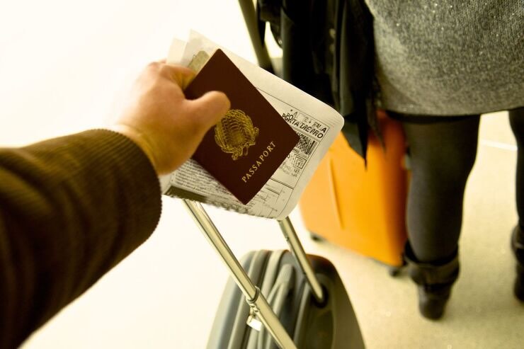 Mano di uomo che tiene manico della valigia e passaporto e biglietto aereo 