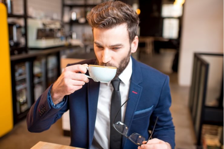 uomo con il vestito e cravatta che beve caffè da tazza bianca