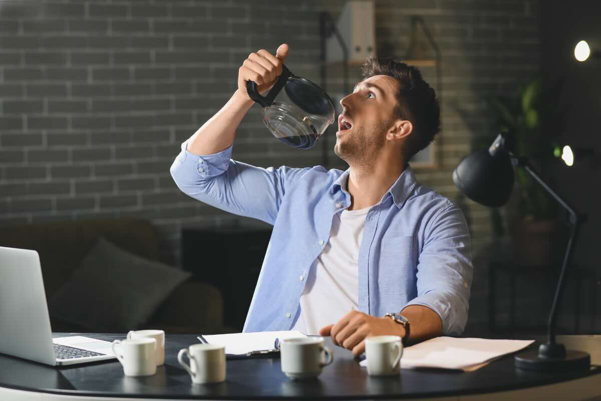 ragazzo con camicia davanti al pc che beve caraffa di caffè