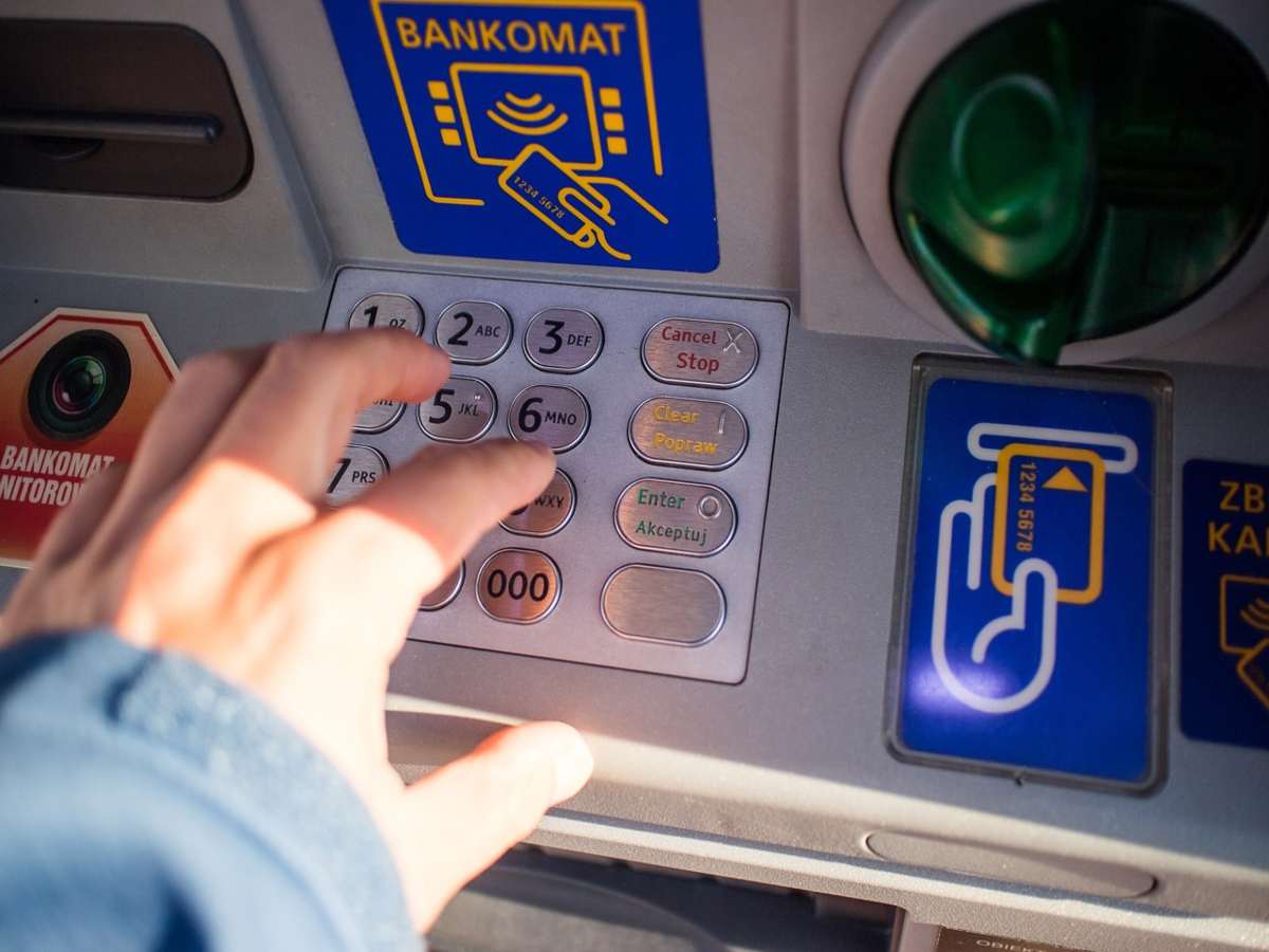 persona che digita il codice numerico sulla tastiera dello sportello bancomat